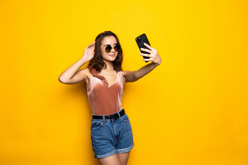 Pretty woman in dress making selfie isolated over yellow background