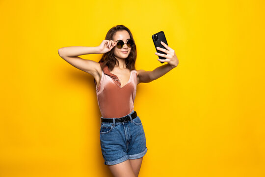 Pretty woman in dress making selfie isolated over yellow background