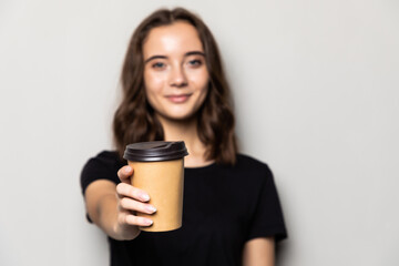 Young beautiful woman offers cup of coffee isolated on gray background