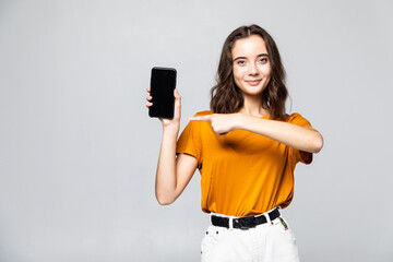 Happy woman in casual clothes showing blank smartphone screen and looking at the camera over grey background