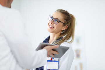 Woman in white coat smiles and communicates with an employee holding tablet in his hands. Positive doctor at work concept