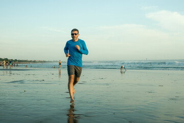 outdoors running workout - young attractive and athletic runner man jogging on beautiful beach in Summer training happy and free in fitness and healthy lifestyle concept