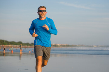 outdoors running workout - young attractive and athletic runner man jogging on beautiful beach in Summer training happy and free in fitness and healthy lifestyle concept