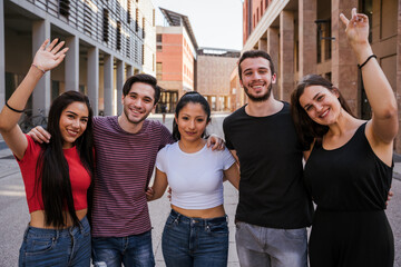 Portrait of a group of friends embraced in the city with hands in the air - Millennials smiling looking the camera - Concept of multiracial team of student in summer time that having fun together - 369063317