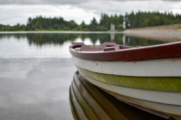 A close up view of a wooden row boat on a calm still lake shore