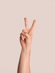 Cropped view of young guy showing victory or peace gesture over light background, close up