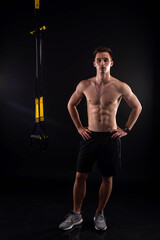Fototapeta na wymiar Young bodybuilder with trx loops on a black background.