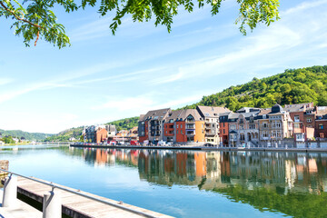 Fototapeta premium image of Dinant in Belgium along the Meuse river with leaves of tree in front of photo. 