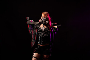 Young woman dressed in a studded leather jacket, gas mask, holding a gun in her hand
