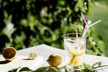 glass with refreshing drink with ice, lemon and straws, on a green background on a wooden surface. Summer drink.