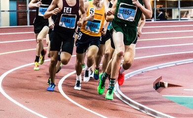 Runners racing on an indoor banked track in a group