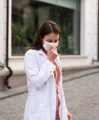 a brunette woman in orange clothes wearing white medical coat and a protective mask on her face