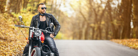 Bearded brutal man in sunglasses and leather jacket sitting on a motorcycle on the road in the...