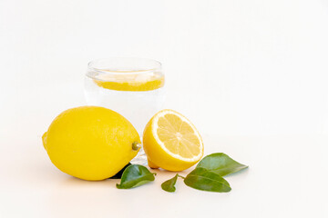 close up of yellow lemon and green limes  with green leaves and glass of water with a piece of lemon inside for refreshment isolated on white background for text.