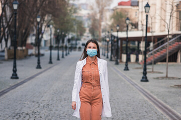 Fototapeta premium a brunette woman in orange clothes wearing white medical coat and a protective mask on her face