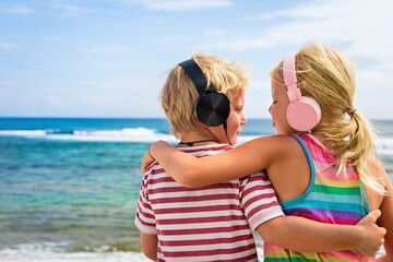 Fototapeta na wymiar Young positive kids in headphones listening music with fun at tropical beach party. Travel family lifestyle, recreational activities at summer cruise vacations.