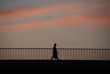 Silhouette of a man with a bag crossing a bridge at sunset