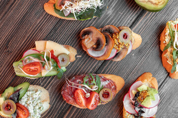 various beautiful bruschettas with vegetables, avocado, salami, cheese, tomatoes, guacamole, olives and radishes 