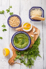 Homemade parsley pesto sauce and ingredients on white  wooden background.