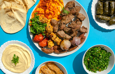 Famous traditional Arabic, Turkish, Israel food. Grilled chicken, lamb, beef, sausages, vegetables, pita bread, tahini sauce, mahshi, stuffed vine leaves, tabbouleh salad on blue background, top view