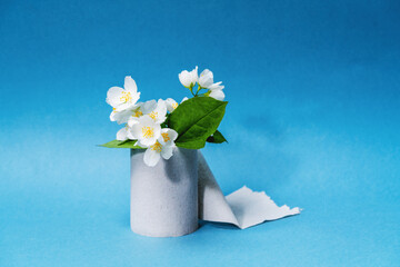 roll of toilet paper and flower of jasmine on a blue background. Toilet paper with a smell