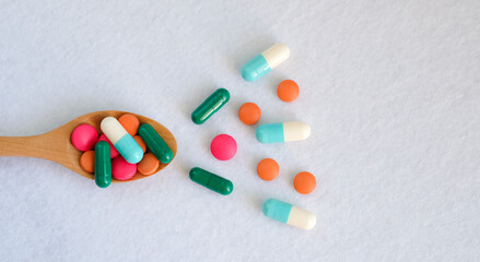 Pills on wooden spoon and scattered over a white background.