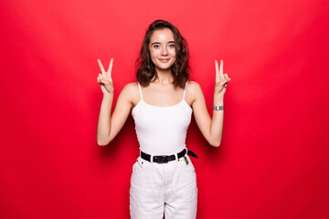 Cheery stylish girl wearing hat showing peace gesture isolated over pink background