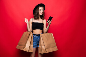 Portrait of young happy smiling woman with shopping bags, with copyspace blank empty area for text or slogan, calling by cell phone, against red background