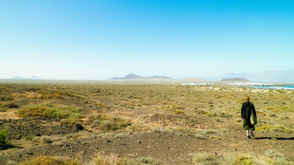 Obraz premium Woman walking across desert close to Caleda de Famara, Lanzarote island.