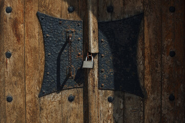 Vintage wooden door with metallic forged handle closed on a padlock