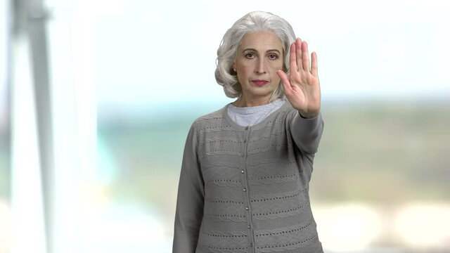 Senior woman making gesture STOP with hand. Elderly caucasian woman saying no with hand sign on blurred background. Defence or restriction.