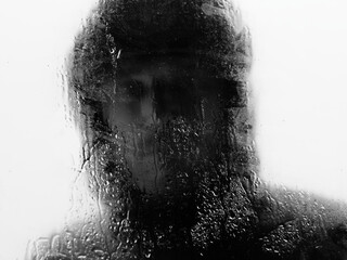 Man outside in raincoat behind wet window during heavy rain. Selective focus. Black and white.
