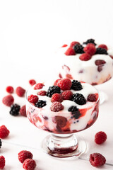 Delicious juicy berries of raspberries and blackberries with yoghurt in a glass form on a white background