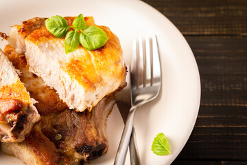 Fried pork entrecote on the bone, cooked pieces of pork meat with basil leaves and spices, cut steak on the bone in a plate on a wooden background