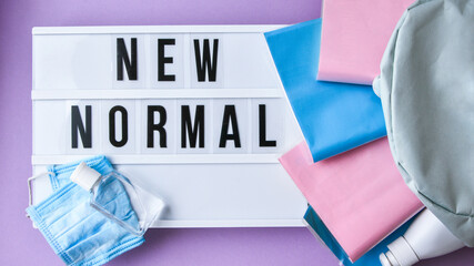 Lightbox with text NEW NORMAL protective face mask and sanitizer. Back to school. Books falling from backpack. Social distancing