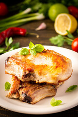 Fried pork entrecote on the bone, cooked pieces of pork meat with basil leaves and spices, steak on the bone in a plate on a wooden background