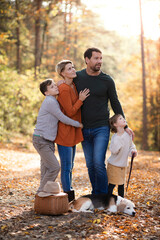Beautiful young family with small children and dog standing in autumn forest.