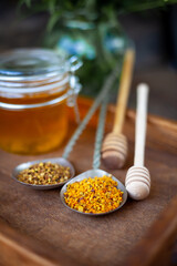 Bee pollen granules. Fresh oney on wooden table. Still life bee product background. Wooden spoon with small glass jar closeup. Eco food. Selective focus, copy space.