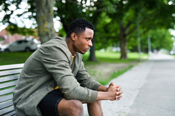 Frustrated young black man sitting on bench outdoors in city, black lives matter concept.