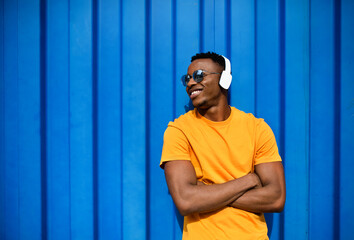 Young black man with headphones standing against blue background, black lives matter concept.