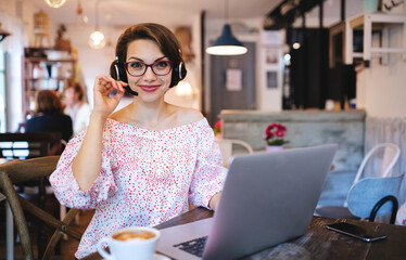 Young woman with headset and laptop indoors in cafe, working.