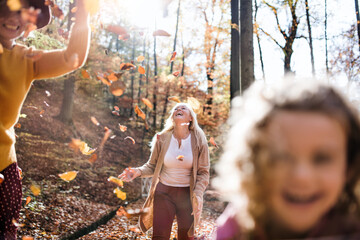Small girl with mother and grandmother on a walk in autumn forest, midsection.