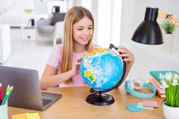 Photo of positive kid girl sit table desk study remote homeschool geography explore globe continent...