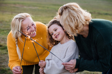 Small girl with mother and grandmother on a walk in nature, holding sparklers.