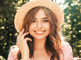 Portrait of young beautiful smiling hipster girl in trendy summer sundress. Sexy carefree woman posing on the street background in the park in hat at sunset. Positive model outdoors