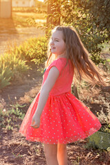 Beautiful smiling little girl with long hair in red dress dancing outdor in sunset. Concept of happy childhood, dancing, holidays. Activities with children summer outdoors. Vertical. © Veronika