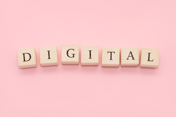 The word DIGITAL is made of wooden cubes on a pink background.