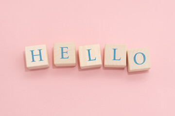 The word HELLO is made of wooden cubes on a pink background.