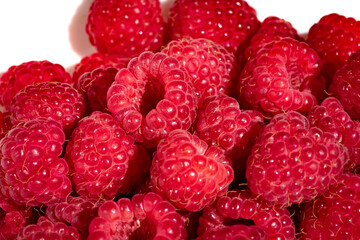 A handful of red ripe raspberries lies on a white plate close-up. Juicy raspberries, macro.