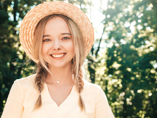 Portrait of young beautiful smiling hipster girl in trendy summer sundress. Sexy carefree woman posing on the street background in the park in hat at sunset. Positive model outdoors